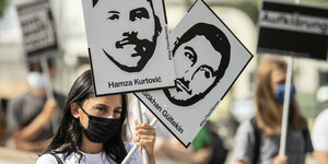 Frau mit Maske hält in Hanau zwei Plakate mit Gesichtern und Namen von Opfern hoch
