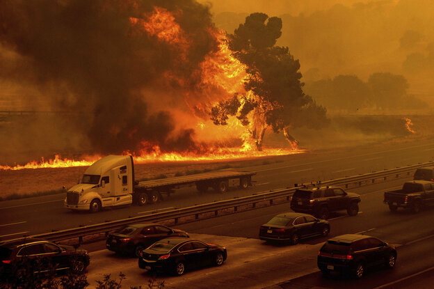Auto sauf einer Autobahn, im Hintergrund ein brennender Wald.