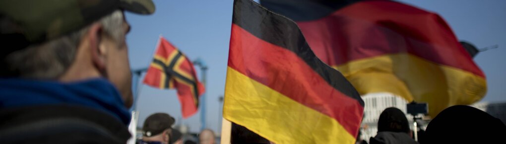 Ein Mann steht auf einer Pegida-Demo neben Deutschlandflaggen