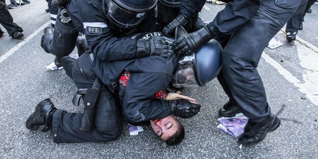 Eine Person wird von der Polizei brutal auf die Straße gedrückt..