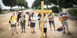 Menschen stehen mit einem Kreuz un dGitarre auf einem Weg.