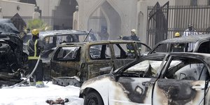 Verbrannte Autos stehen vor einer Moschee. Feuerwehrmänner löschen.