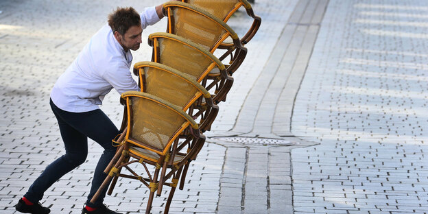 Ein Mann hält einen kippenden Stapel Stühle fest.