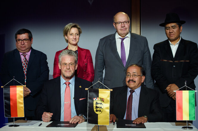 Gruppenfoto auf dem Altmaier und Wolfgang Schmutz bei der Vertrgsunterzeichnung zu sehen sind. Auf dem Tisch vor ihnen stehen kleine Landesfahnen