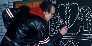 Keith Haring zeichnet mit Kreide Herzen und Männchen an eine Tafel