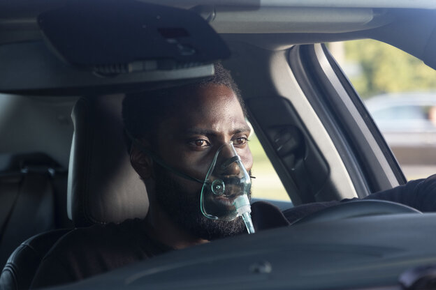 Ein Mann sitzt in einem Auto, über Mund und Nase eine mit einem Schlauch verbundene Maske Ein Mann sitzt in einem Auto, über Mund und Nase eine mit einem Schlauch verbundene Maske