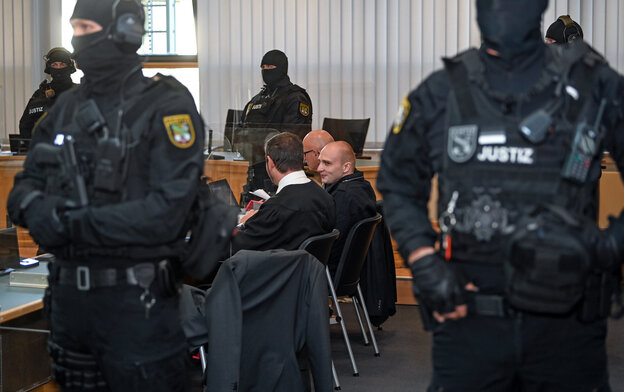 Bewaffnete Polizisten bewachen eine Person in einem Gerichtssaal. Bewaffnete Polizisten bewachen eine Person in einem Gerichtssaal.