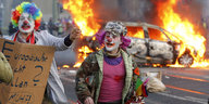 Als Clowns verkleidete Demonstranten und ein brennendes Auto