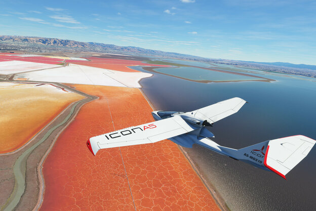 Ein Flugzeug fliegt über rote und orangene Felder, die an ein Gewässer grenzen