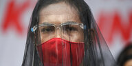 Eine Frau trägt einen Trauerschleier und einen roten Mundschutz