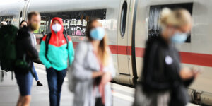 Menschen mit Masken auf einem Bahnsteig vor einem ICE.