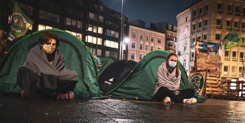 Zwei Personen sitzen vor zwei Zelten