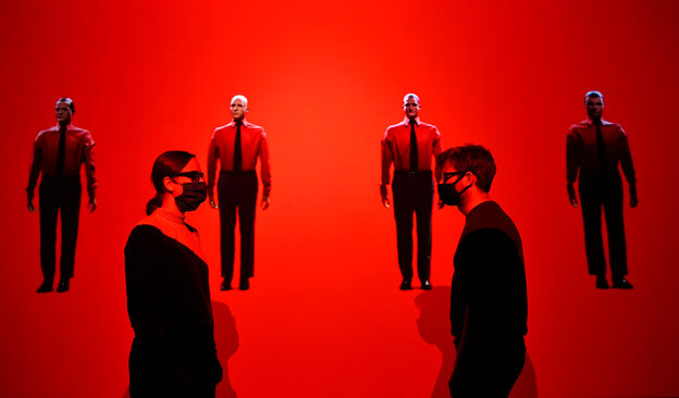 Galerie-Assistenten tragen lange schwarze Pullover und stehen in einer Ausstellung, die mit dunkelrotem Licht durchflutet ist Galerie-Assistenten tragen lange schwarze Pullover und stehen in einer Ausstellung, die mit dunkelrotem Licht durchflutet ist
