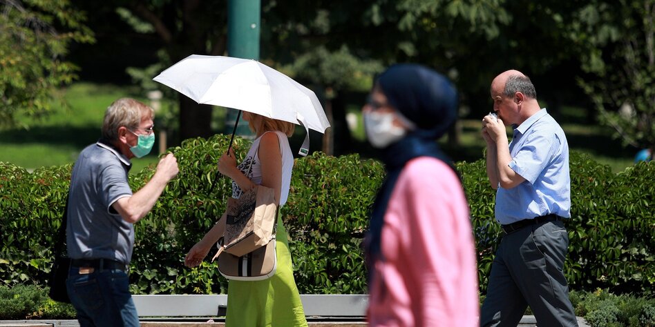 Maskenträger laufen an einem sonnigen Tag durch den Park in Sarajewo