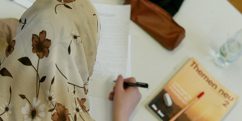 Frau mit Kopftuch macht sich Notizen im Unterricht an einer Berliner Volkshochschule