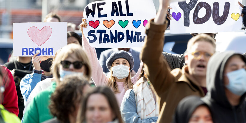 Menschen stehen vor dem Gericht und halten Schilder hoch, etwa mit Aufschriften wie "We all stand with you"