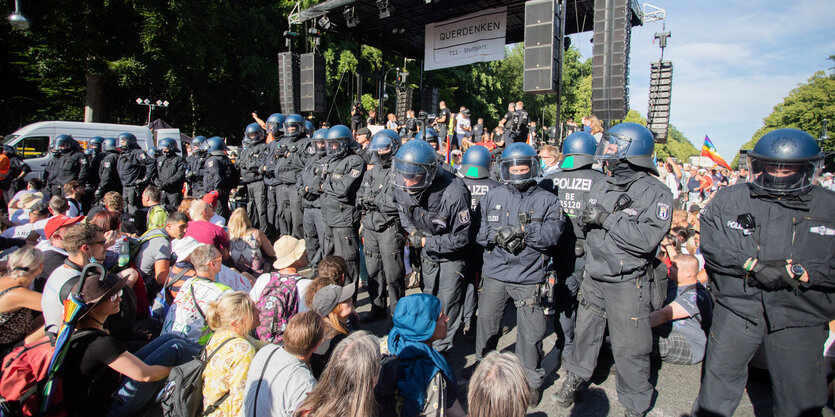 Menschen sitzen vor einer Polizeikette