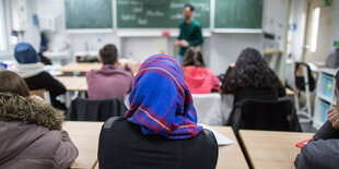 Eine Schülerin mit kopftuch sitzt in der letzten Reihe und blickt zur Tafel