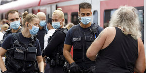 Polizisten tragen Schutzmasken und stehen einem Mann gegenüber