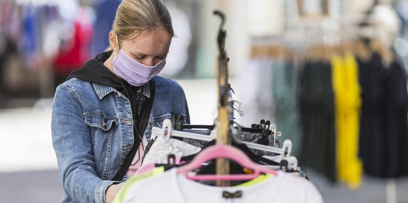 Eine Frau trägt einen Mundschutz und schaut sich Kleidung an, die auf einem Kleiderständer hängt