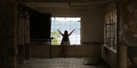 Eine Frau steht mit ausgebreiteten Armen an einem vergitterten Fenster. Es ist eine Touristin auf der ehemaligen Gefängnisinsel Goli Otok