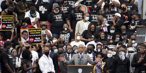 Reverend Al Sharpton steht am Rednerpult, umringt von Menschen in Schwarzen T-Shirts mit der Aufschrift "I can't breathe" und der Zahlenkombination 8:46
