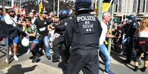 Rückenansicht eines Polizisten vor einer Menschenmenge, aus der heraus versucht wird, Sperren zu durchbrechen