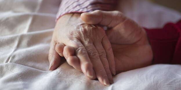 Die Hand einer Pflegerin hällt die Hand eines sterbenden Mannes
