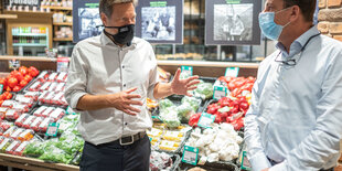 Robert Habeck redet gestikulierend mit Maske vor einem Gemüseregal mit einem Mann in weißem Hemd