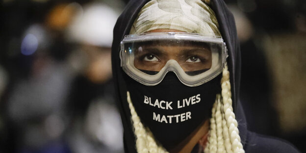 Ein Demanstarnt trägt eine Schutzbrille und einen Mund-Nasen-Schutz mit der Aufschrift "Black Lives Matter"