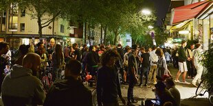 Junge Menschen sitzen und stehen bei Dunkelheit vor einem Kiosk.