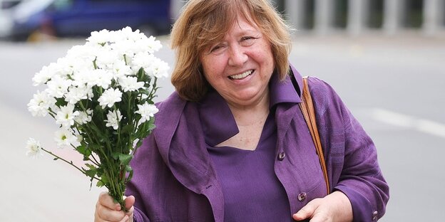 Die belarussische Schriftstellerin Swetlana Alexijewitsch lächelt und hält einen Blumenstrauß in die Höhe.