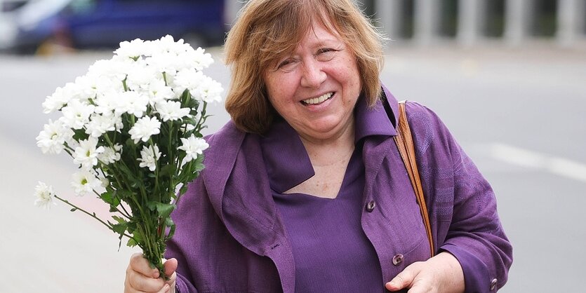 Die belarussische Schriftstellerin Swetlana Alexijewitsch lächelt und hält einen Blumenstrauß in die Höhe.