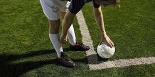 Ein Ball liegt auf der Markierung auf einem Fussballfeld mit Kunstrasennem Fußball.