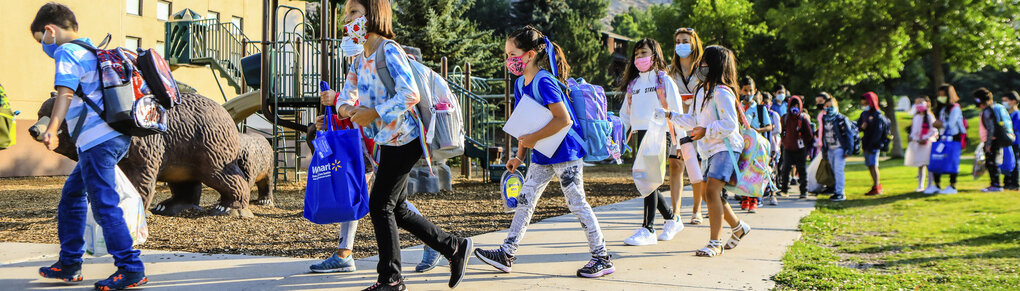 Kinder mit Masken und Taschen auf dem Weg zur Schule