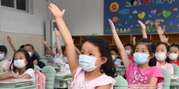 Chinesische Mädchen mit Mundschutz recken eine Hand in die Höhe