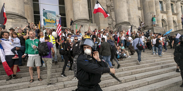 Ein POlizist mit SChlagstock, hinter ihm eine Menschenmenge auf der Treppe vor dem Reichstagsgebäude