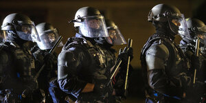 Polizisten in martialischen Uniformen und mit Schutzhelmen stehen im Dunkeln