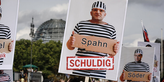 Schilder mit Bildmontagen, die Gesundheitsminister Jems Spahn und den bayerischen Ministerpräsidenten Markus Söder in Sträflingskleidung zeigen