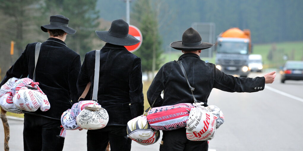 Drei Zimmergesellen im Zunftgewand stehen mit Stock und Hut an der Bundestraße 31 und versuchen per Anhalter weiter zu kommen.