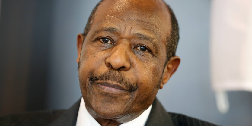 Paul Rusesabagina, ein alter Mann mit Oberlippenbart. Er hat eine sehr hohe Stirn und an den Seiten über den Ohren kurze Haare. Er trägt einen Anzug.