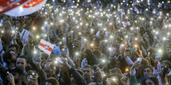 Belarussische DemonstrantInnen versammeln sich im Dunkeln und leuchten mit ihren Smartphone. Es wehen Flaggen der Protestbewegung