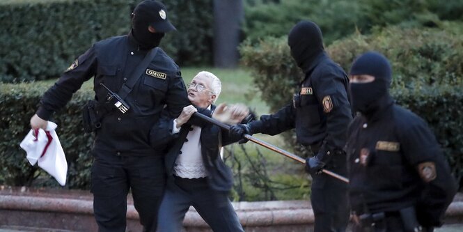 Polizisten in martialischen Uniformen entreissen einer alten frau eine weiß-rote Fahne