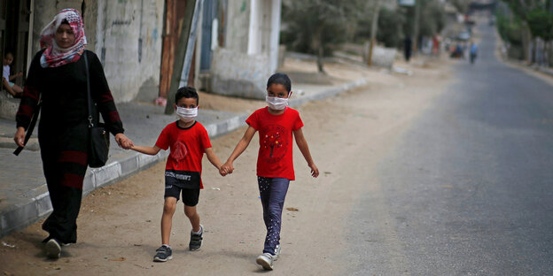 Zwei Kinder in roten T-shirts und ihre Mutter gehen eine Straße entlang