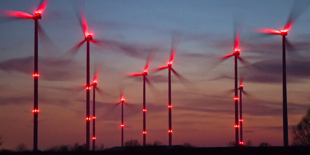 Rot blinkende Positionslichter an Windrädern vor Abendhimmel