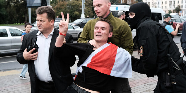 Ein junger Mann mit Victory-Zeuchen und einehüllt in eine belarussische Flagge wird abgeführt