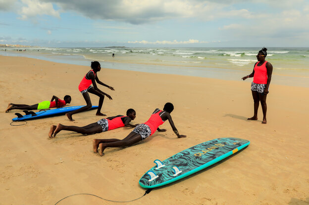 Mädchen üben am Strand mit ihren Surfbrettern, davor gibt die Lehrerin Anweisungen