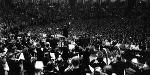 Ein Dirigent inmitten einer Menge von Musikern und Konzertbesuchern
