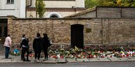 Menschen stehen vor der Mauer der Synagoge, vor der viele Blumen abgelegt wurden