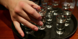Eine Hand greift in einer Gaststätte nach einem gefüllten Schnapsglas.